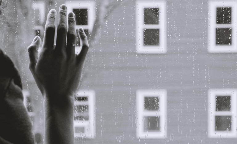 Black and white photo of a hand on a window with rain drops on it