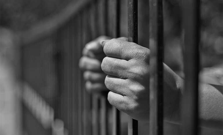 Hands on rail of jail cell