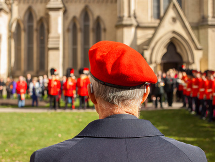 Veteran wearing a red beret watching a military ceremony outside a stone church.