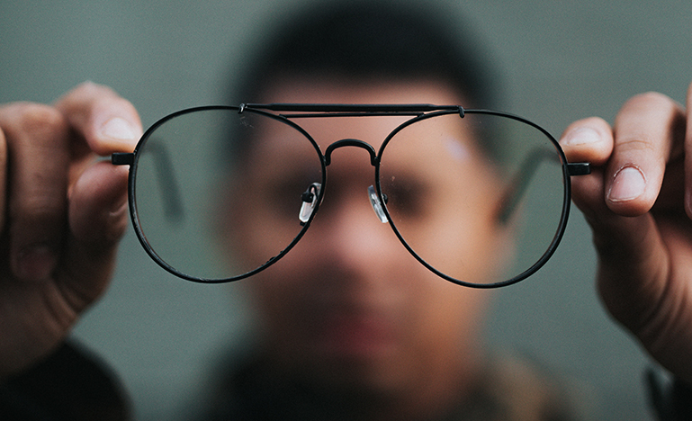 Image of a blurry person holding up a pair of glasses
