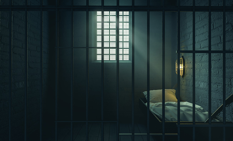 Dimly lit prison cell with metal bars and a small bed