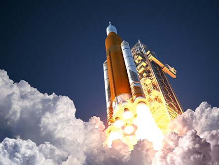 A large rocket launches, surrounded by billowing clouds of smoke and bright flames, against a clear blue sky, conveying power and excitement.