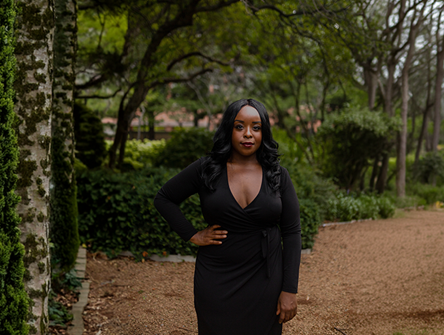 Woman in black dress standing in a garden path among trees.
