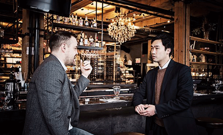 Deux hommes vêtus de complets en pleine conversation dans un bar