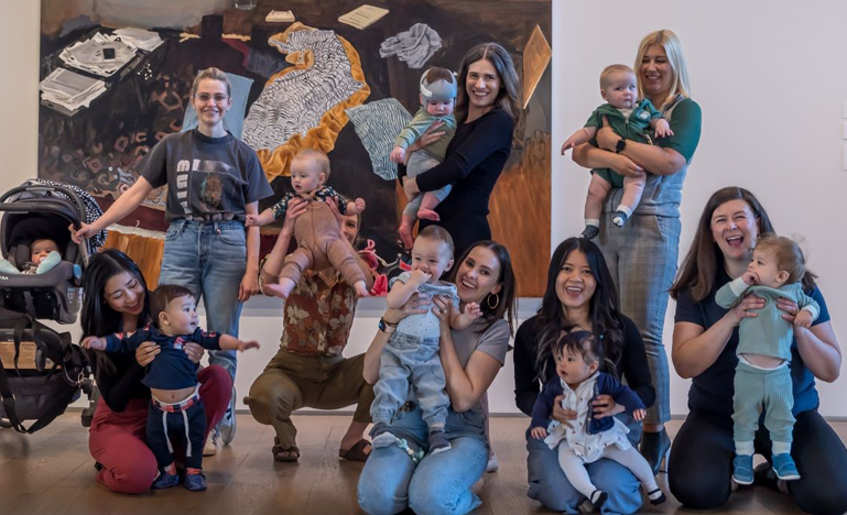 A group of women laywers and their children pose in front of a peice at an art gallery