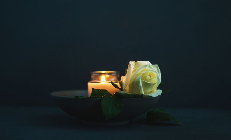 A burning candle with a white rose in remembrance