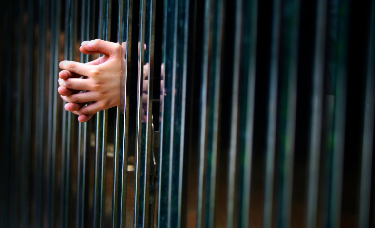 Hands gripping the metal bars of a prison cell