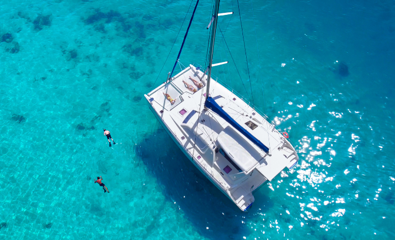Aerial view of people snorkelling near a catamaran anchored in blue Caribbean water