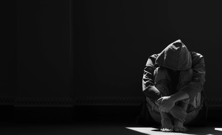 A person crouches alone in the dark