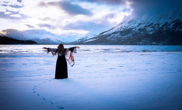 An Indigenous woman stands in the snow near a mountain lake