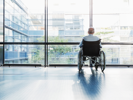 Senior Man in Wheelchair looking out of a window in a care facility corridor