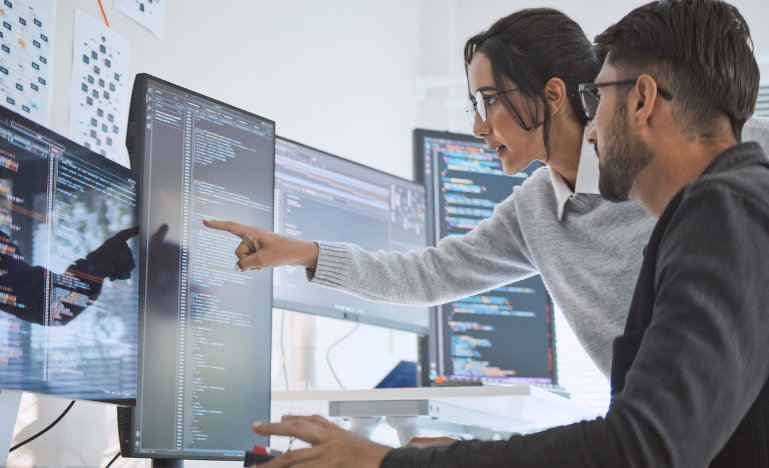 A man and a woman working on multiple computer monitors