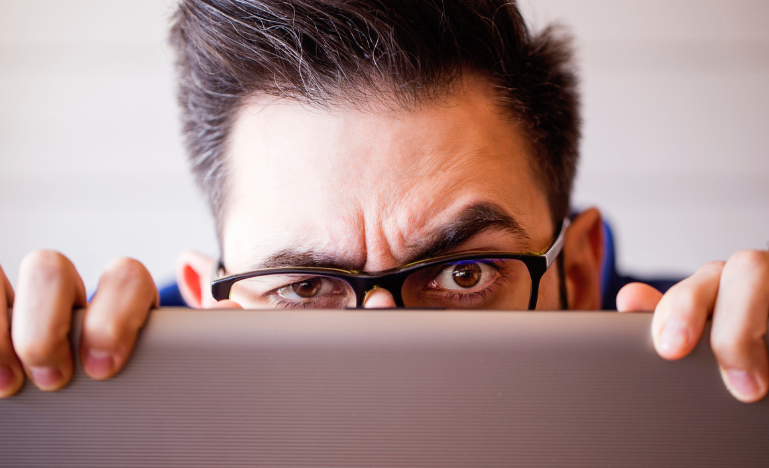 A man peeks over the top of laptop computer