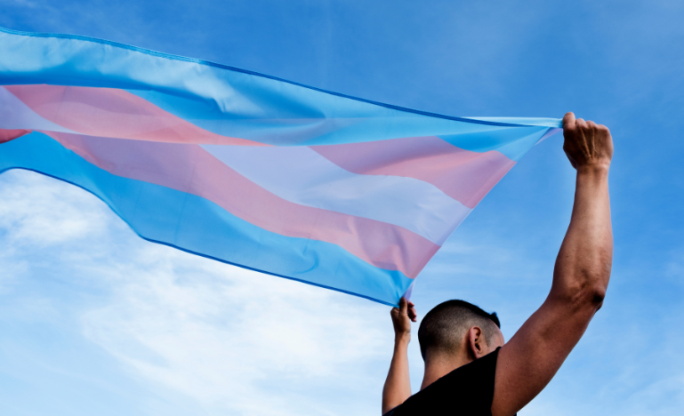 A man holds a transgender pride flag over his head