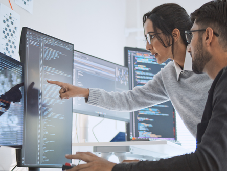 A man and a woman working on multiple computer monitors